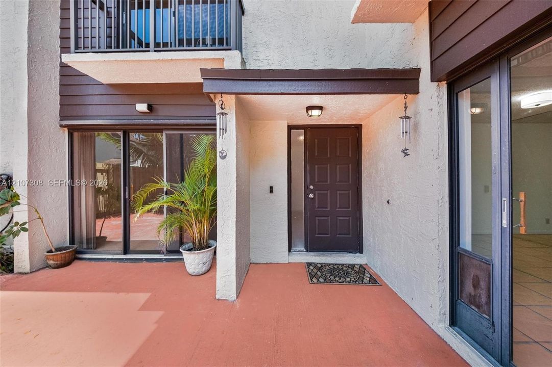 Covered entryway featuring a paneled door with side-light, second-story balcony with metal railing, stucco exterior, and dual sliding glass door access