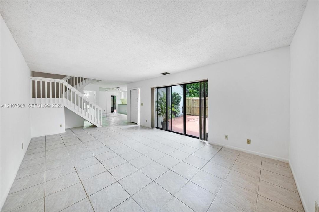 Open interior space featuring light-toned tile flooring, white staircase with balustrade, and sliding glass doors