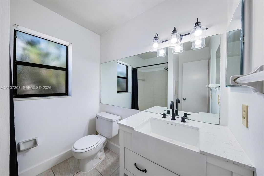 White vanity with a rectangular integrated sink, quartz-style countertop, matte black widespread faucet, large wall-mounted mirror, and multi-light vanity fixture