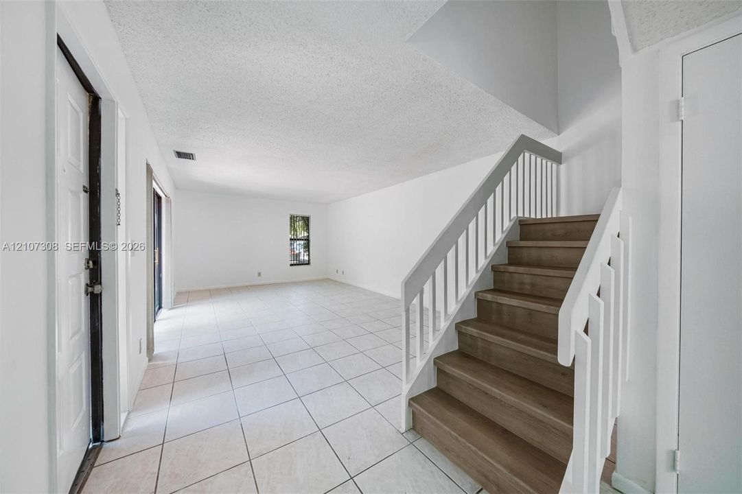 Interior space featuring light-toned tile flooring, a staircase with wood-finish treads, and white balustrade railings