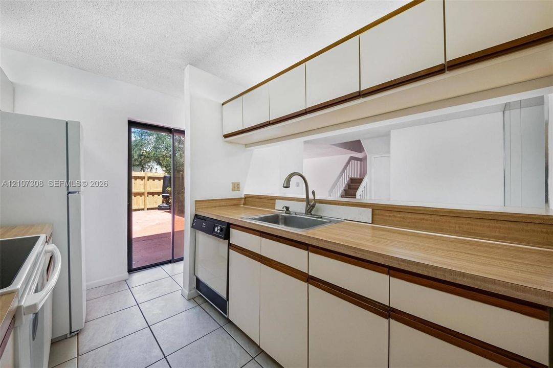 Kitchen featuring cabinetry with wood-tone accents, integrated dishwasher, stainless steel sink with high-arch faucet, and tile flooring
