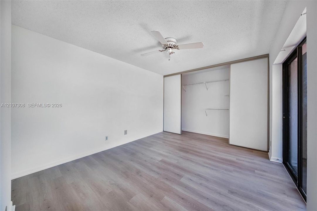 Wood-finish flooring, ceiling fan, sliding closet doors with built-in shelving, and sliding glass door