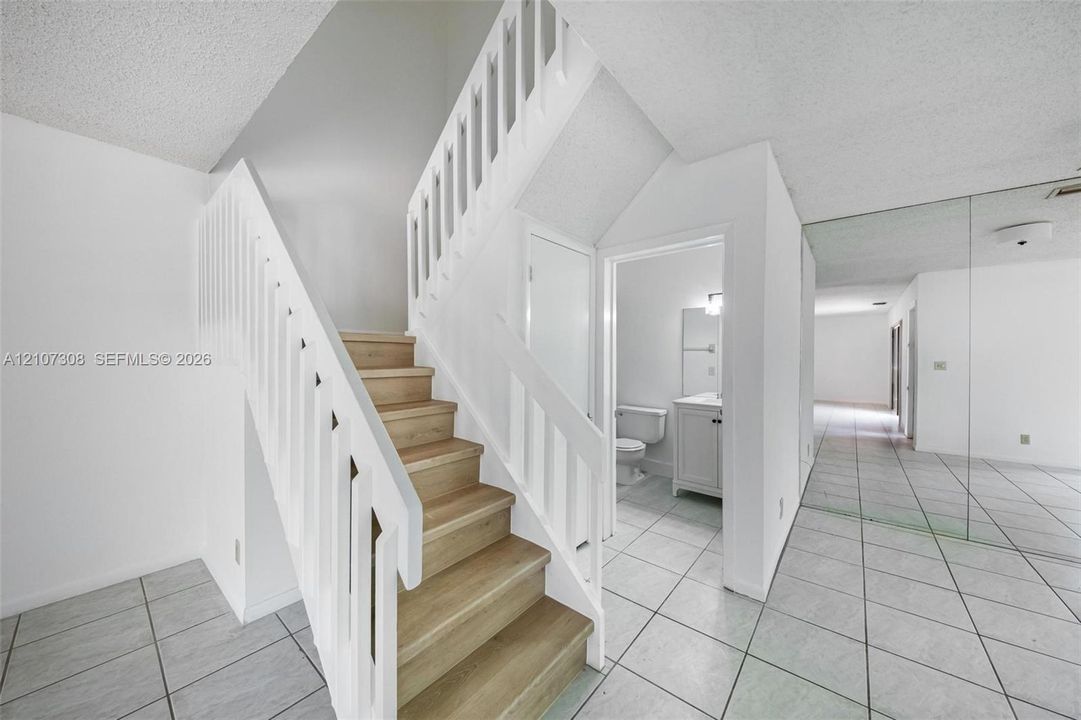 Staircase featuring white balusters and wood-finish treads, complemented by neutral tile flooring and a wall-mounted mirrored panel