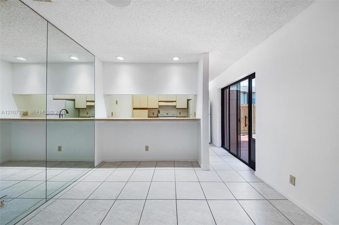 Tile flooring, full-wall mirror, kitchen pass-through with flat-surface ledge, and sliding glass door