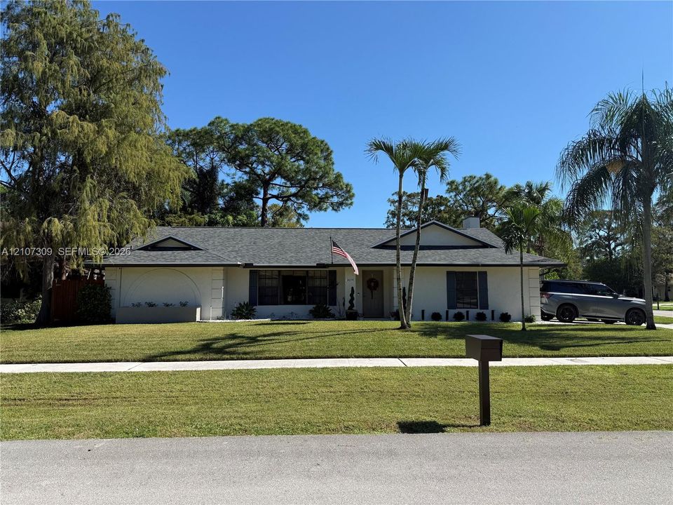 Single-story exterior featuring a light-toned stucco façade, a shingled roof, contrasting window shutters, and established palm trees
