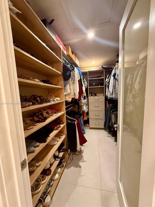 Walk-in closet featuring extensive built-in shelving, integrated dresser drawers, hanging rods, and large-format tile flooring