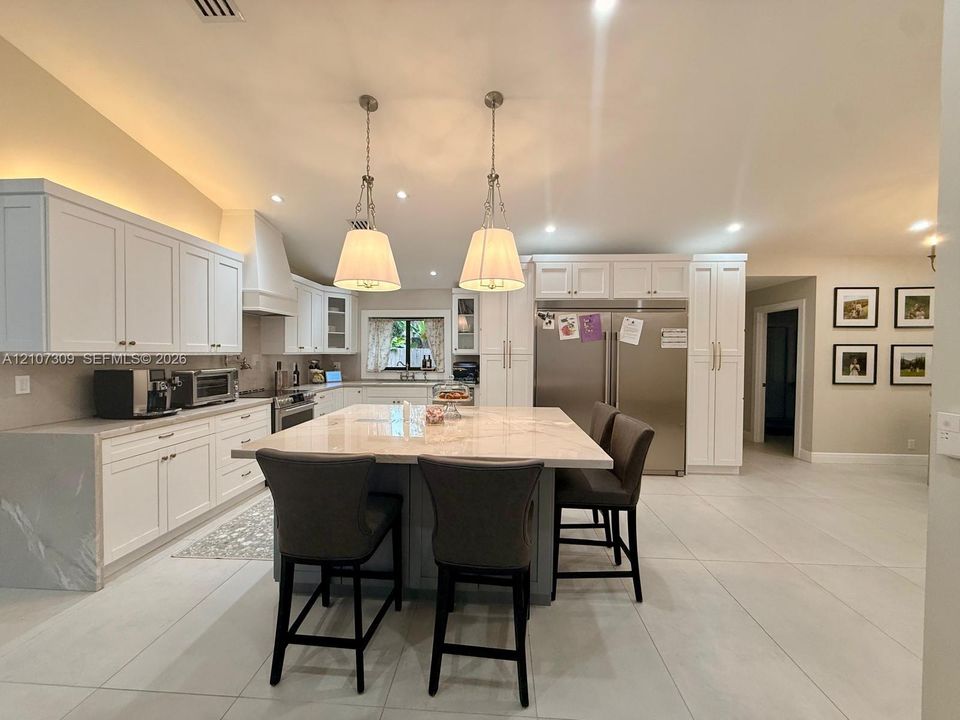 Kitchen featuring white cabinetry, a central island with a stone countertop, stainless steel refrigerator, stone-style flooring, and dual pendant lighting