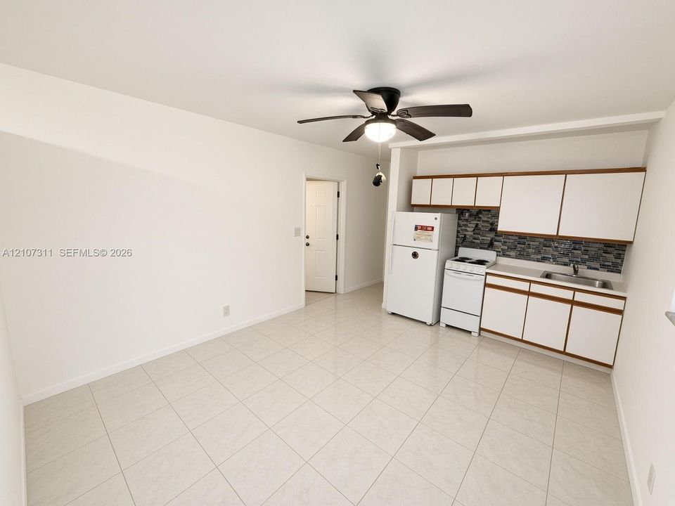 Neutral tile flooring, white cabinetry, textured stone-finish backsplash, built-in ceiling fan, and white appliances