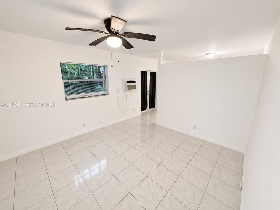 Interior space featuring large-format ceramic tile flooring, a ceiling fan with integrated lighting, a single-hung window, and a wall-mounted air conditioning unit