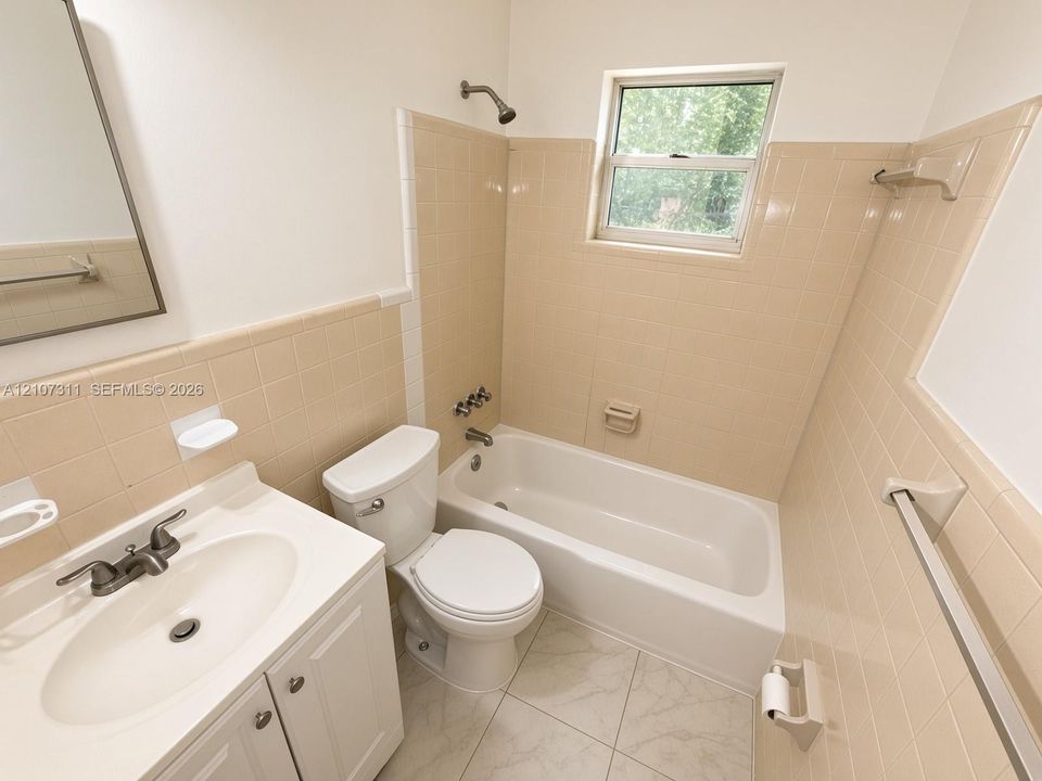 Bathroom featuring a white vanity cabinet with an integrated sink, porcelain bathtub with showerhead, ceramic tile wall surround, and large-format floor tiling