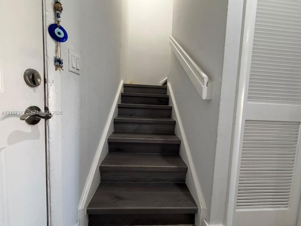 Staircase featuring wood-finish treads and a white wall-mounted handrail, complemented by a louvered-panel closet door