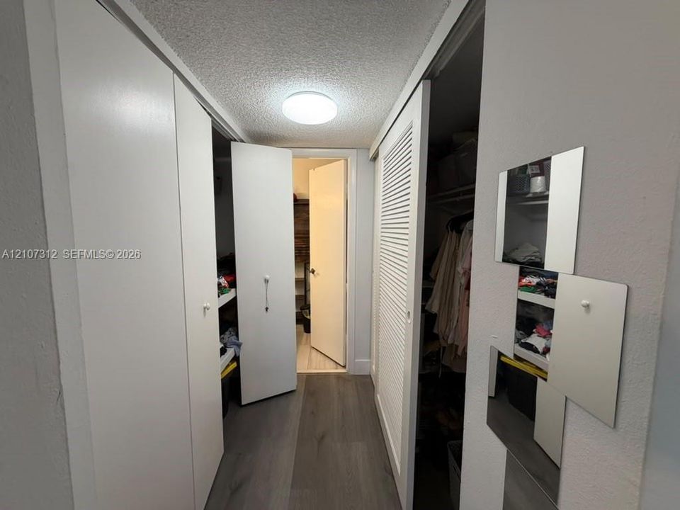 Hallway featuring wood-finish flooring, flush-mount ceiling lighting, bi-fold closet doors, and louvered storage doors