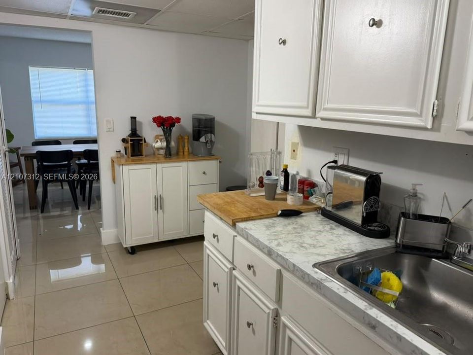 Kitchen featuring white cabinetry, stone-patterned laminate countertops, stainless steel sink, and light-toned tile flooring