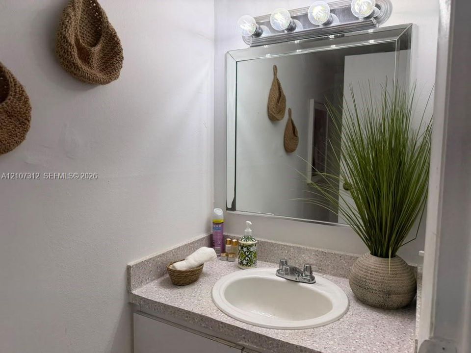 Vanity featuring a stone-composite countertop, integrated oval basin, polished chrome faucet, and a large beveled-edge mirror with a multi-bulb light fixture