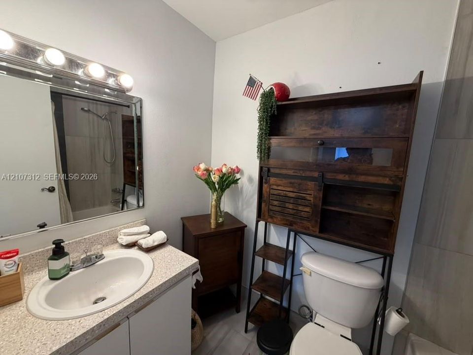Bathroom featuring a vanity with an integrated basin, a speckled composite countertop, a framed wall mirror, and a multi-bulb vanity light fixture