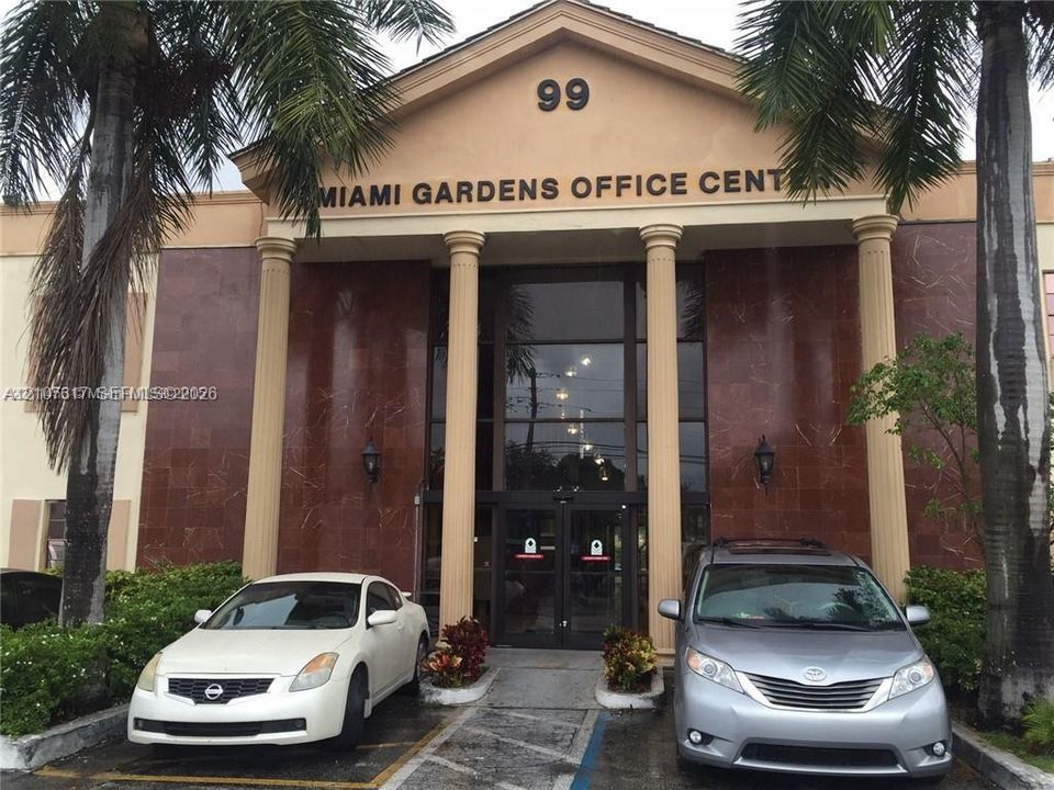 Commercial exterior featuring a pedimented roofline, full-height decorative columns, natural stone facade panels, and a glass-enclosed entrance