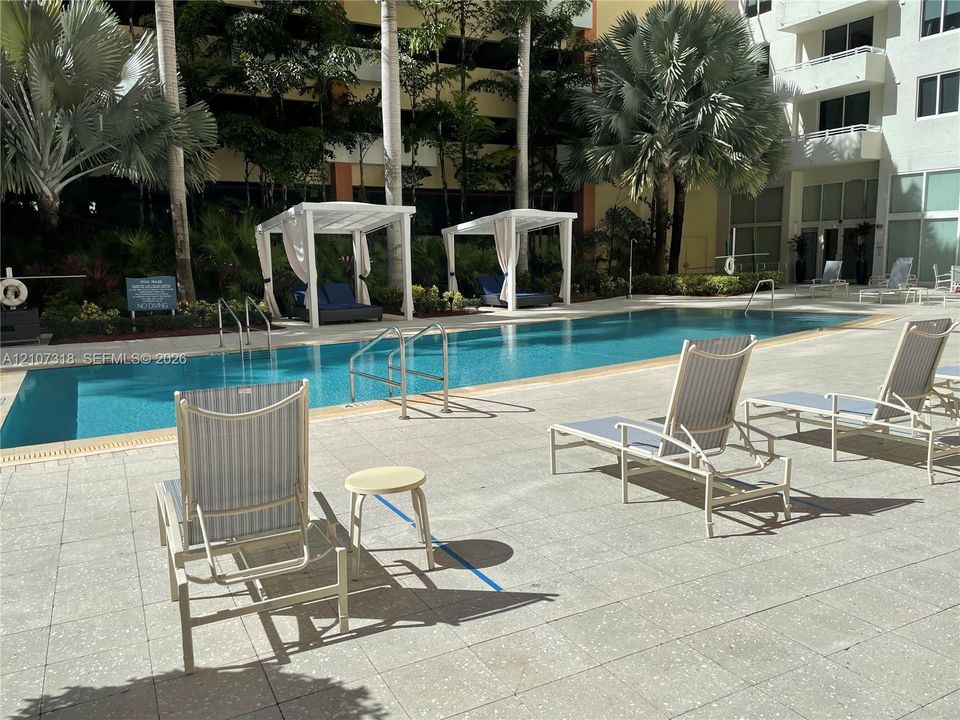 Rectangular swimming pool featuring a tiled deck, metal railings, and built-in poolside cabanas accented by mature palm trees