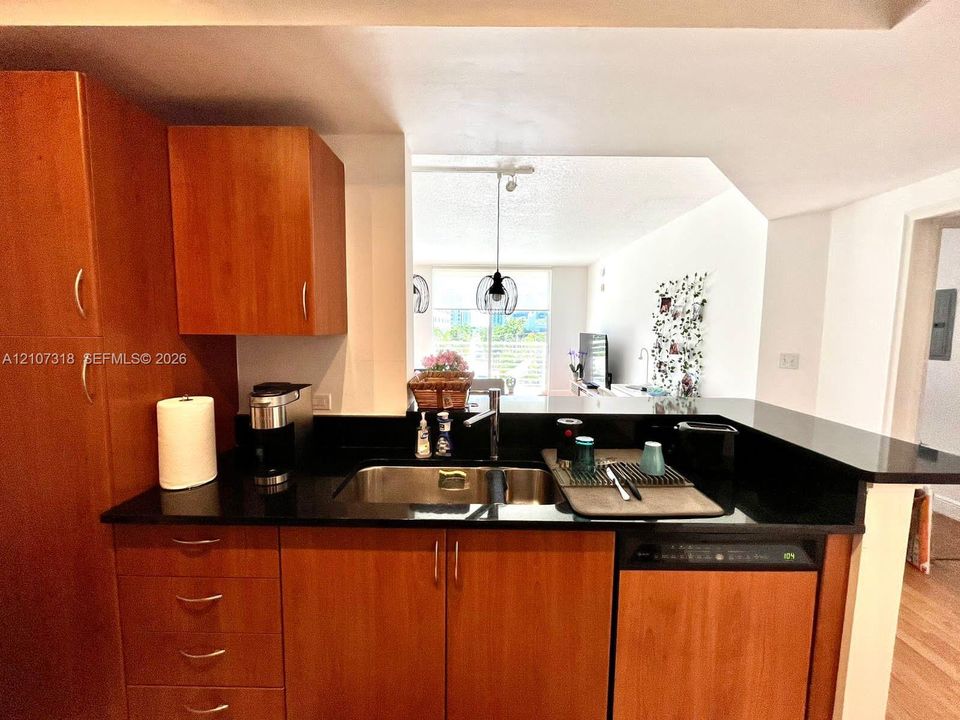 Kitchen featuring wood-finish cabinetry, dark solid-surface countertops, a dual-basin stainless steel sink with a high-arch faucet, and an integrated dishwasher