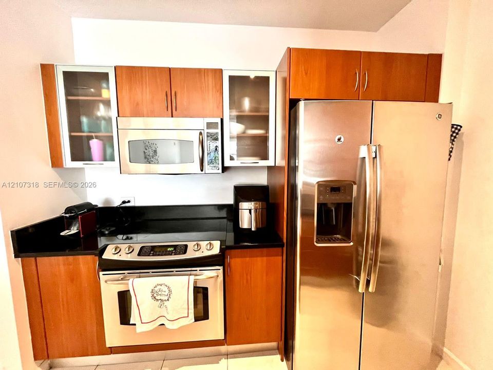 Kitchen area featuring wood-finish cabinetry, black countertops, stainless steel appliances, and glass-paneled upper cabinet doors