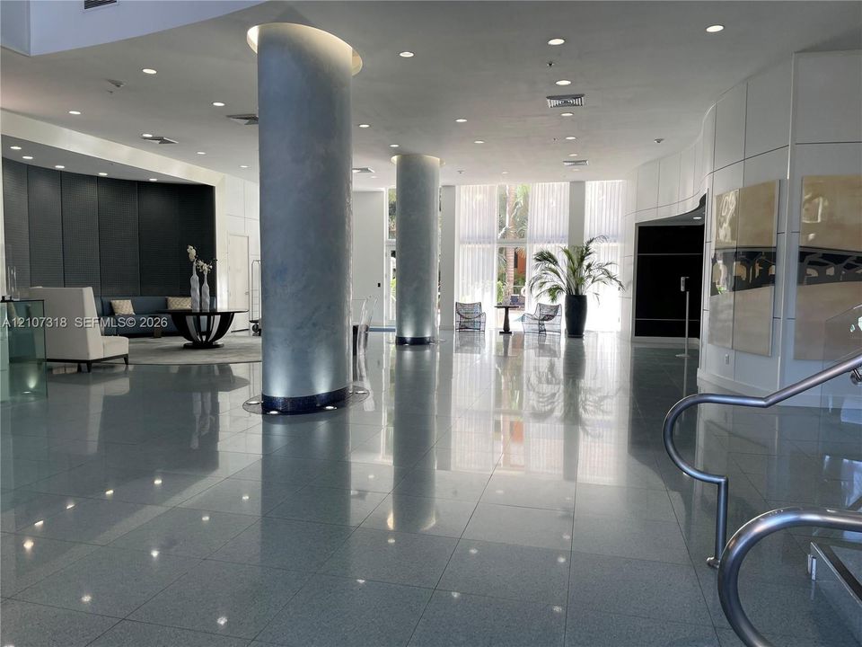 Grand foyer featuring polished stone flooring, dual floor-to-ceiling structural columns, recessed lighting, and expansive floor-to-ceiling glass windows