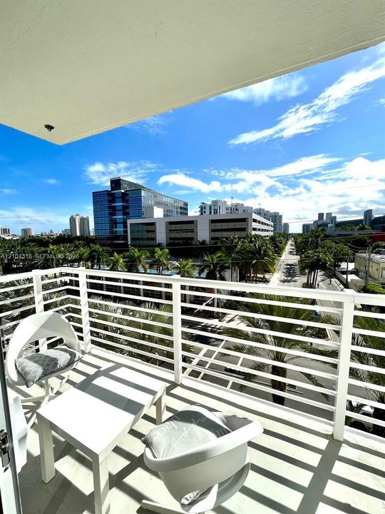 Covered balcony featuring white aluminum railings and concrete flooring, overlooking an urban cityscape with mature palm trees