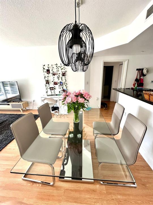 Geometric matte black pendant lighting fixture over a dining area featuring wood-finish flooring and a kitchen peninsula with a dark stone countertop