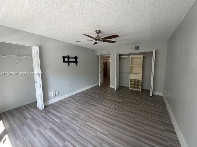 Room featuring wood-finish flooring, a ceiling fan, and dual closets with built-in shelving
