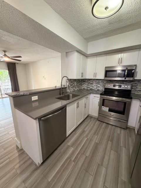 Kitchen featuring stainless steel appliances, solid-surface countertops, decorative tile backsplash, white shaker-style cabinetry, and wood-finish flooring