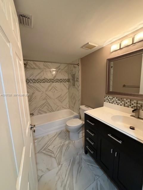 Bathroom featuring a vanity with dark cabinetry and a white countertop, patterned wall and floor tile, a tiled tub surround with a decorative mosaic accent border, and a framed vanity mirror with integrated lighting