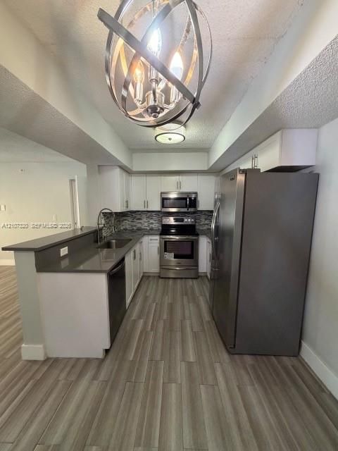 Kitchen featuring white cabinetry, quartz countertops, stainless steel appliances, wood-finish flooring, and a spherical metal chandelier