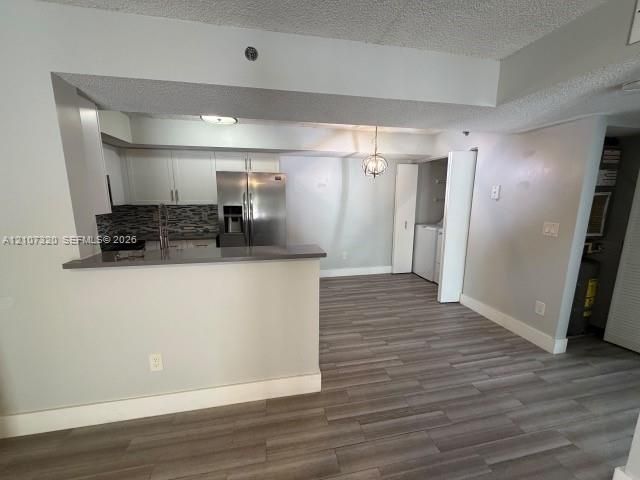 Kitchen featuring white cabinetry, solid-surface countertops, stainless steel refrigerator, and wood-finish flooring