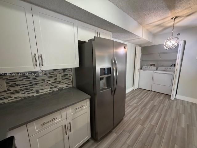 Kitchen featuring white shaker-style cabinetry, a multi-tonal linear tile backsplash, stainless steel side-by-side refrigerator, solid-surface countertops, and wood-finish flooring
