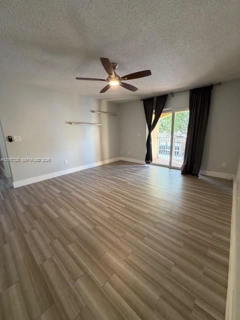 Interior space featuring wood-finish flooring, a ceiling fan with integrated lighting, wall-mounted shelving, and a sliding glass door providing external access