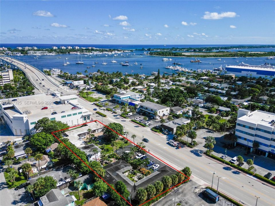 Aerial perspective of property featuring a multi-structure footprint, paved parking areas, established palm trees, and perimeter landscaping