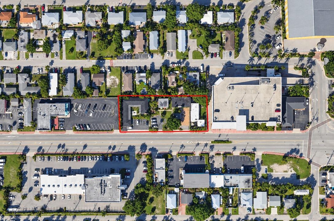 Aerial perspective of a multi-structure property featuring surface parking, paved driveways, established trees, and direct street frontage