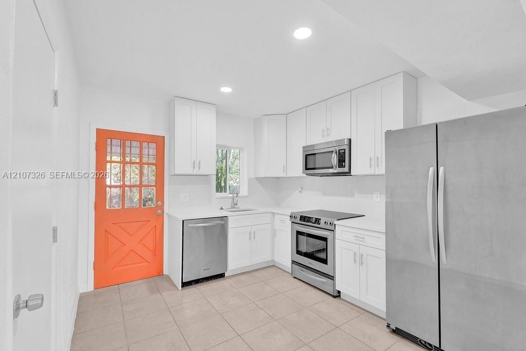 Kitchen featuring white shaker-style cabinetry, solid-surface countertops, stainless steel appliances, tile flooring, and a glass-paneled exterior door