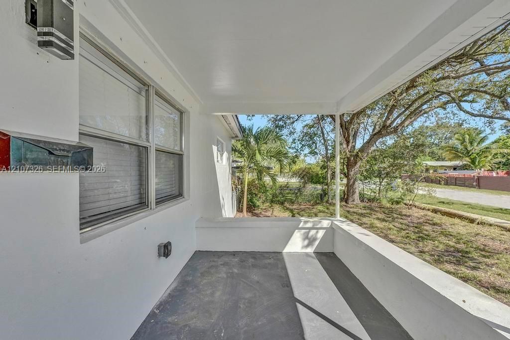 Covered porch featuring concrete flooring, a smooth white ceiling, exterior wall-mounted lighting, and a metal mailbox