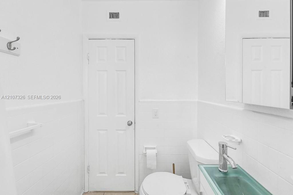 White subway tile wall cladding, single-panel interior door, medicine cabinet with mirrored front, and glass vessel sink with chrome-finish faucet
