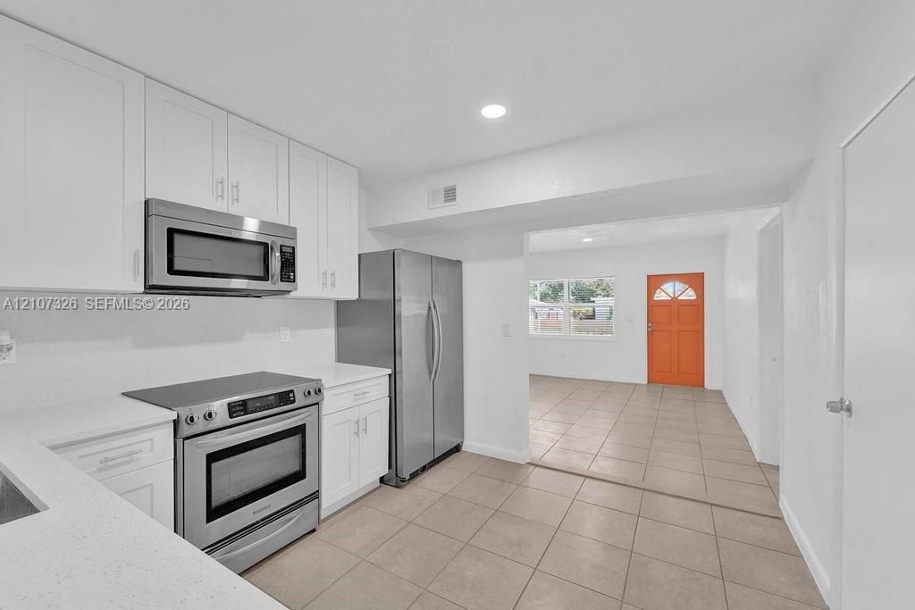 Kitchen featuring white cabinetry, solid-surface countertops, and stainless steel appliances including a built-in microwave, range, and refrigerator