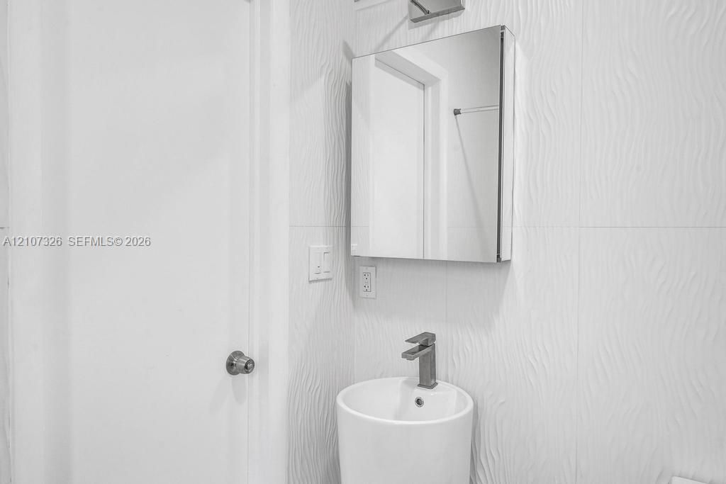 Wall-mounted medicine cabinet with a mirror, cylindrical pedestal sink, single-lever faucet, and textured tile wall cladding