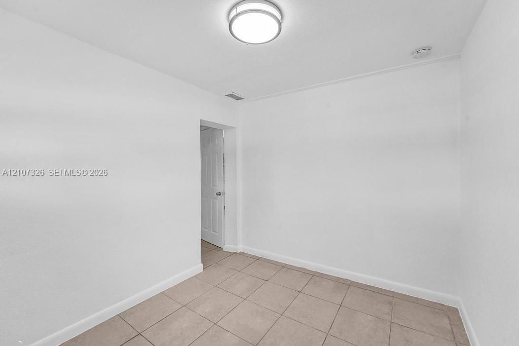 Interior room featuring neutral ceramic tile flooring, crisp white walls, and a circular flush-mount ceiling light fixture