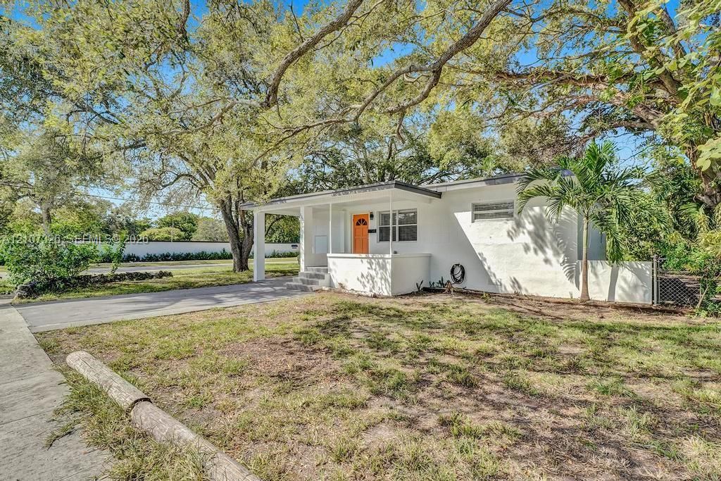 Single-story residence featuring a painted masonry exterior, covered front porch, concrete driveway, and mature landscaping