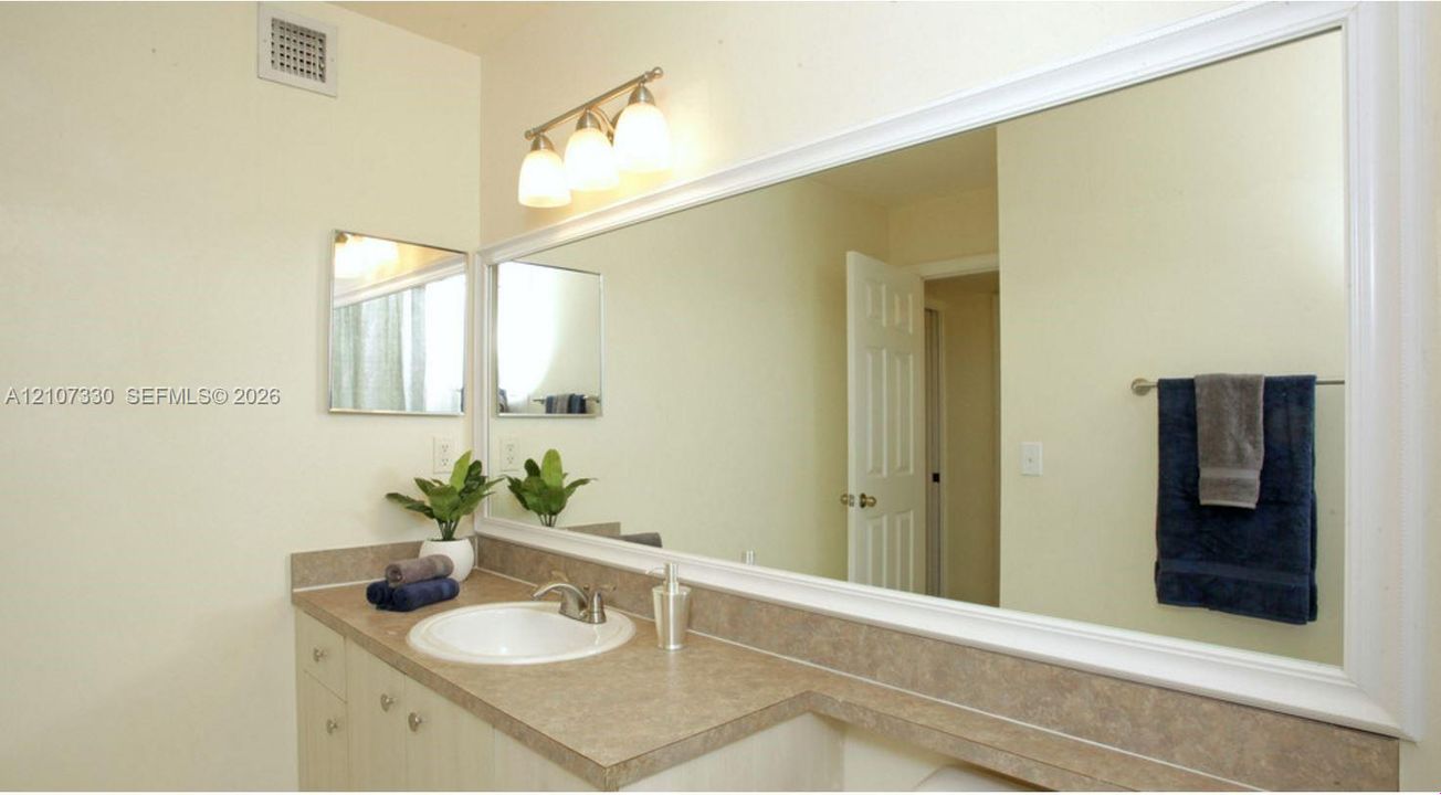 Vanity featuring a solid-surface countertop, integrated basin, three-light fixture, and an expansive wall-mounted mirror with a white frame