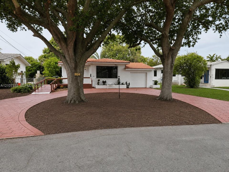 Stucco exterior residence featuring a clay tile roof, circular paver driveway, and mature trees