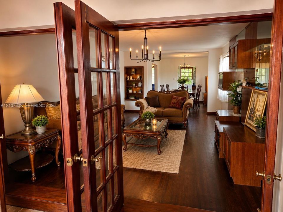 French doors with glass paneling, wood-finish flooring, built-in recessed shelving, and a chandelier with multi-arm lighting