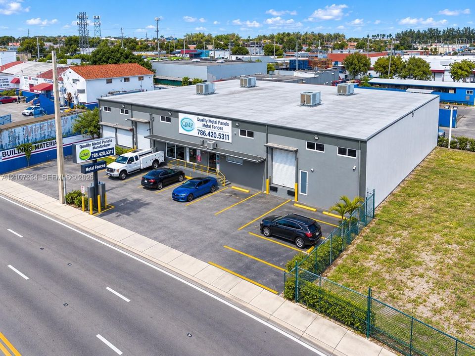 Commercial property featuring a concrete exterior, asphalt parking area with marked stalls, roll-up loading door, and perimeter chain-link fencing