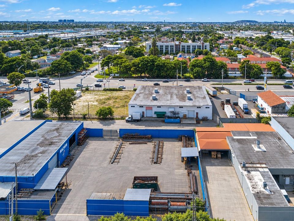Industrial property featuring an expansive gated paved yard, secure perimeter wall, multiple metal warehouse structures, and direct street access