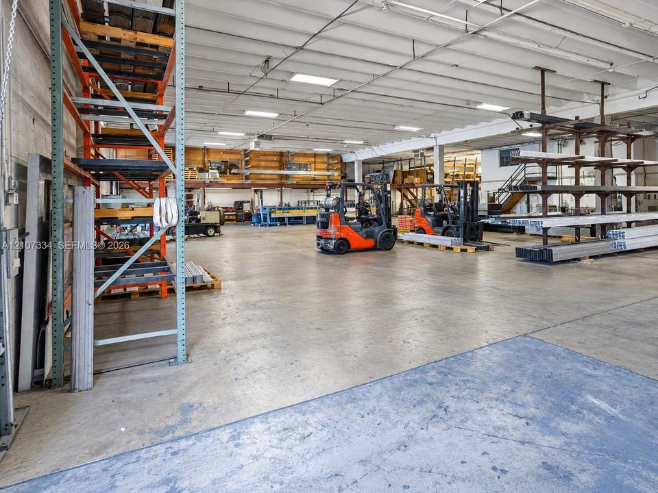 Industrial warehouse space featuring high ceilings, polished concrete flooring, extensive built-in steel racking systems, and overhead lighting