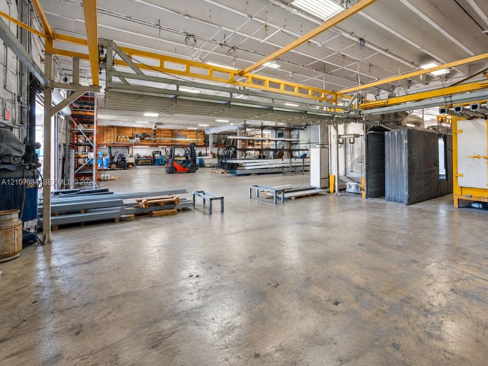 Industrial warehouse space featuring concrete flooring, an exposed structural ceiling, integrated overhead gantry cranes, and high-clearance open floor plan
