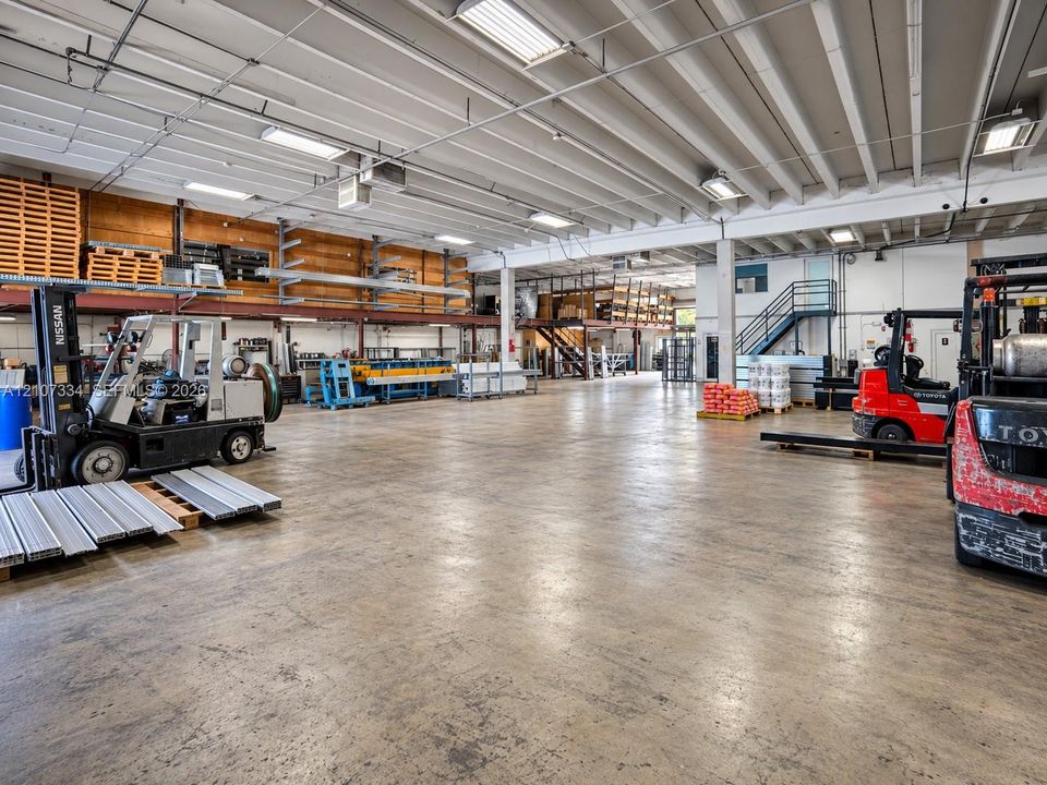 Expansive industrial warehouse featuring polished concrete flooring, exposed overhead beams, mezzanine storage platform, integrated lighting, and steel staircase access